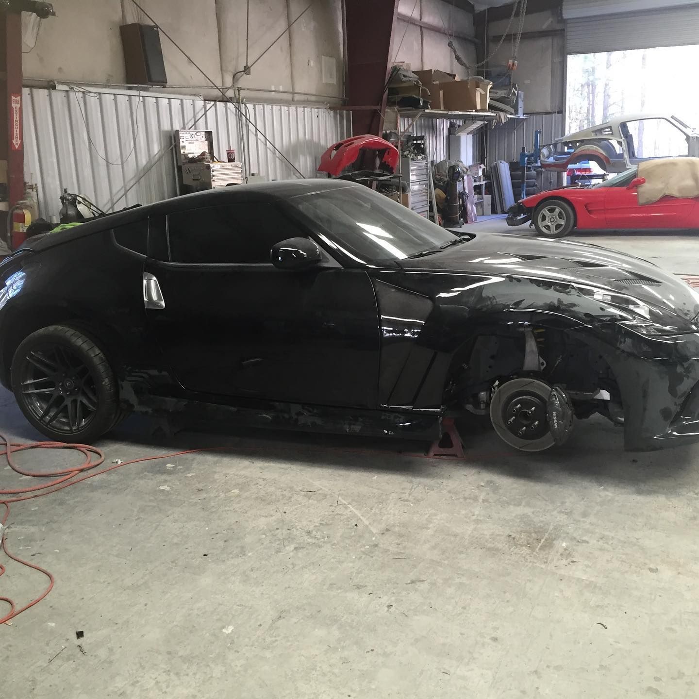 Black sports car in a repair shop with its front end disassembled.