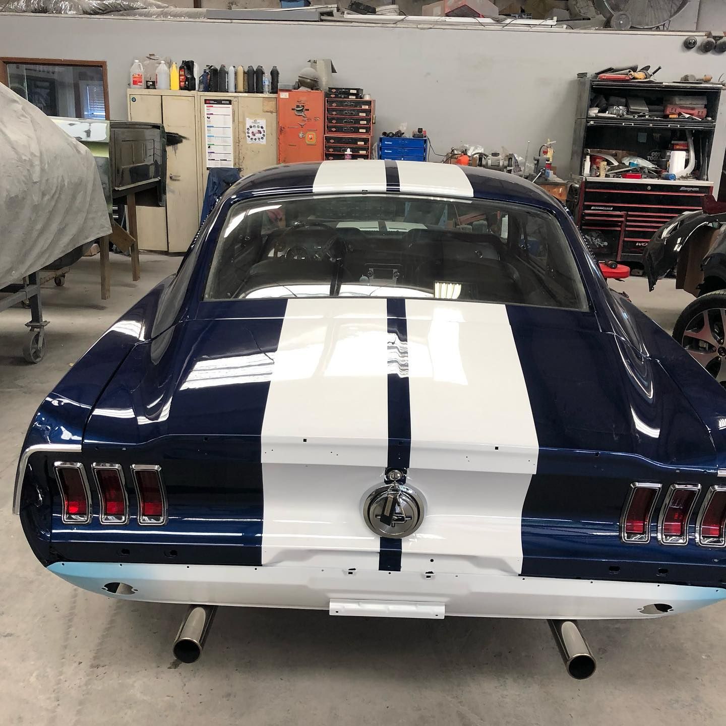 Blue Mustang car with white stripes, inside a garage.