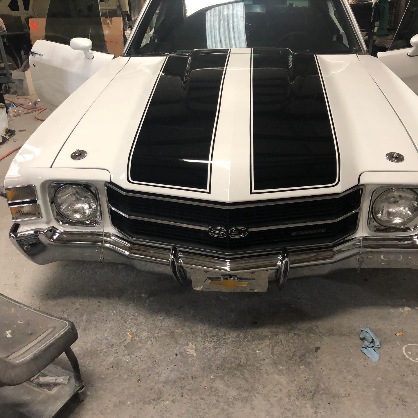White classic car with black racing stripes and open doors in a workshop.