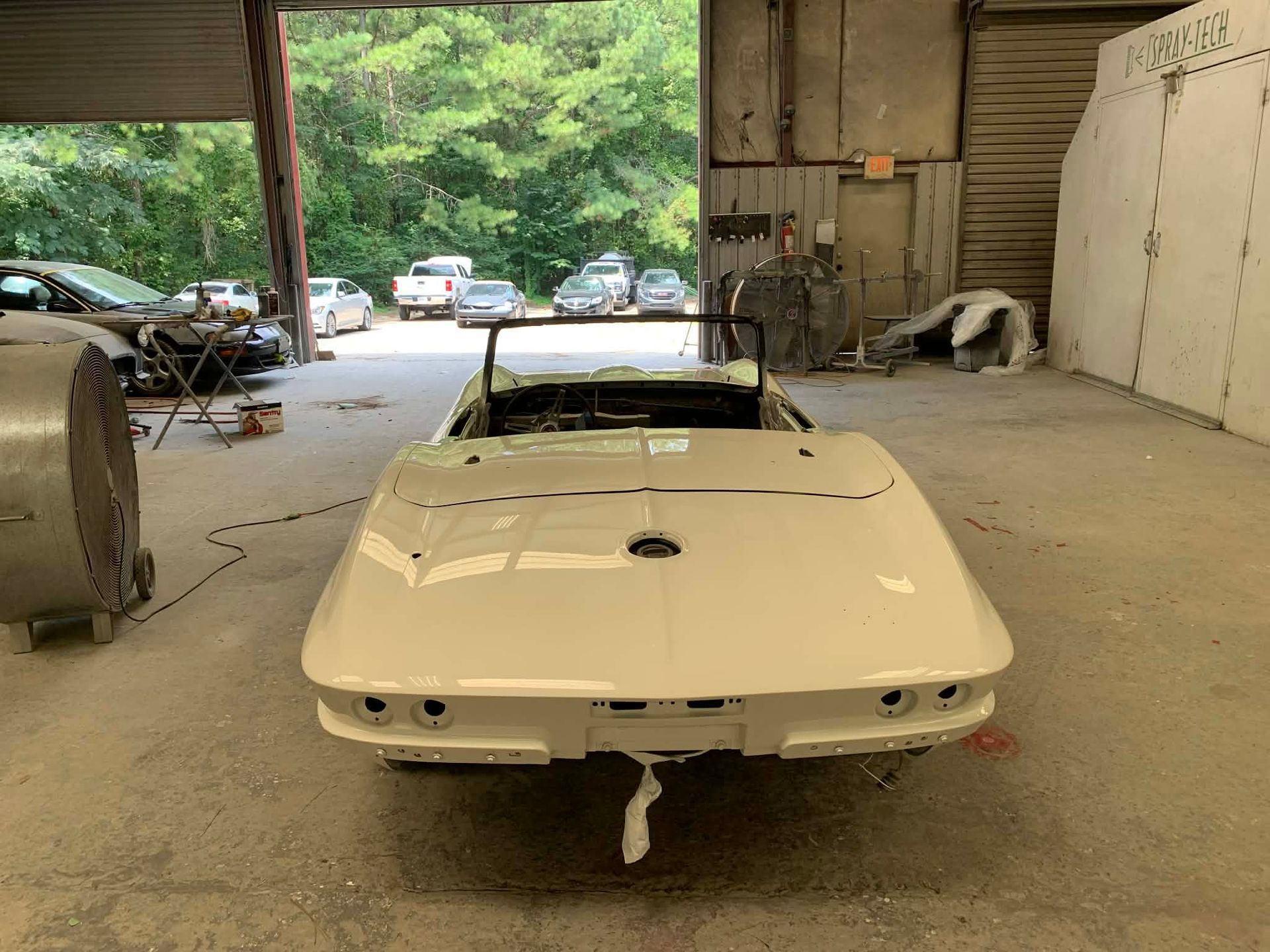 White classic car body in a workshop garage with a tow hook and open bay doors.