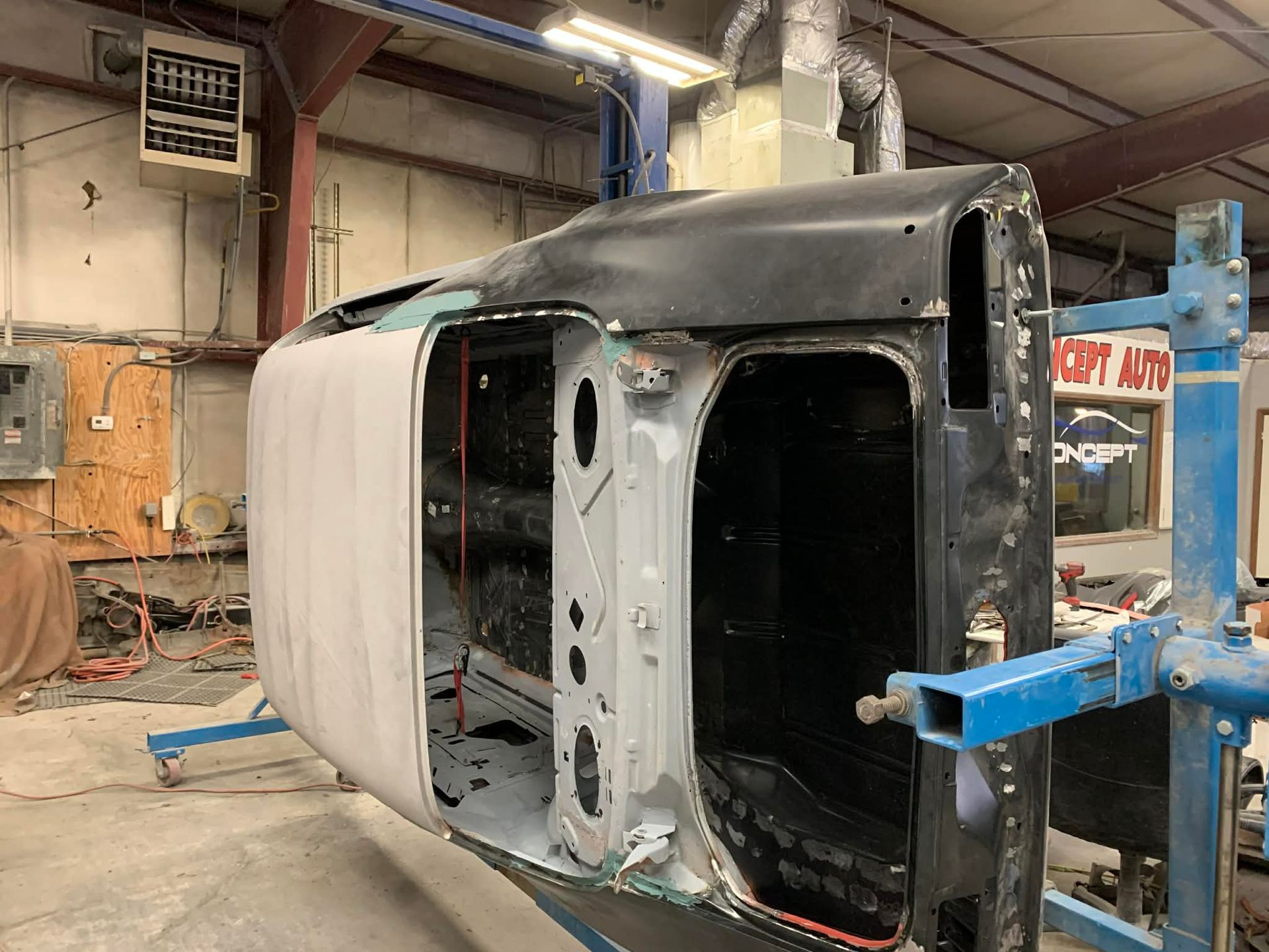 Damaged black vehicle body in an auto repair shop, mounted on a blue frame with exposed interior.