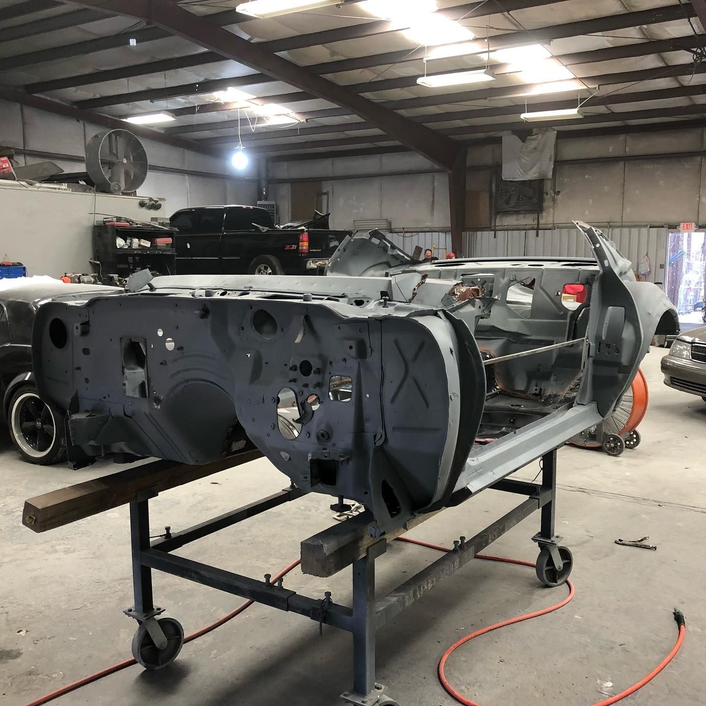 Partially disassembled car body on a wheeled stand inside a workshop, ready for restoration.