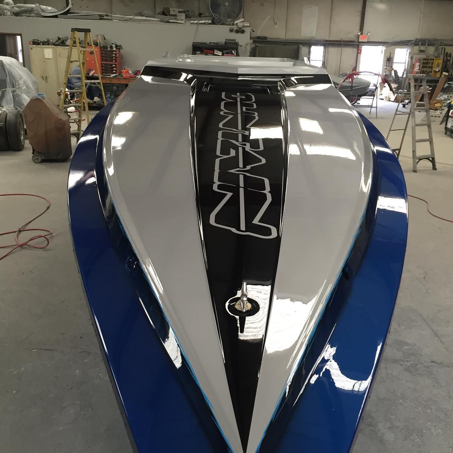 Blue and white speed boat with black accent on the bow, in a workshop setting.