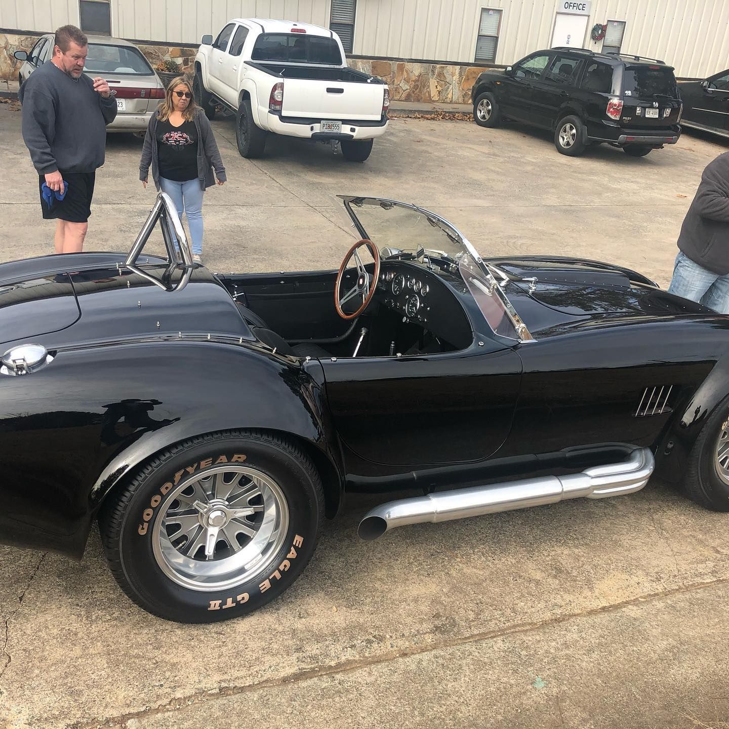 Black Cobra convertible car parked, onlookers present outdoors.