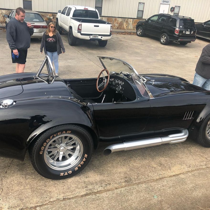 Black Cobra convertible car parked, onlookers present outdoors.