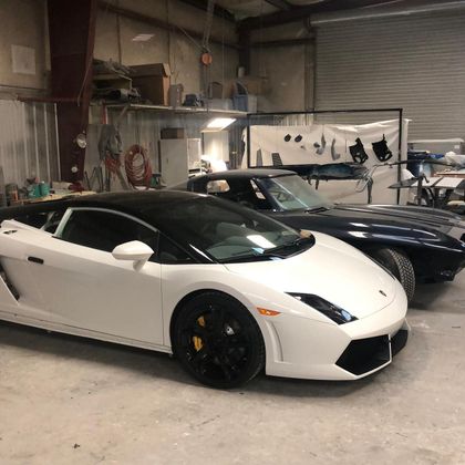 White Lamborghini with black roof parked beside a dark blue sports car in a garage.