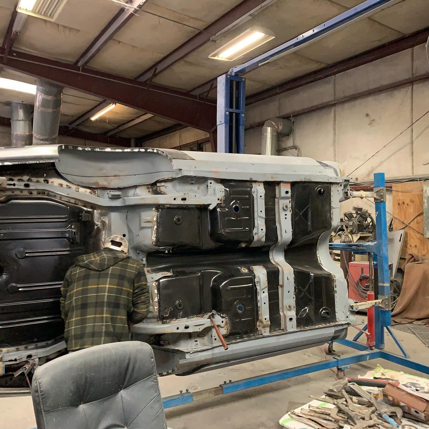 Car chassis being worked on in a workshop with a person welding.
