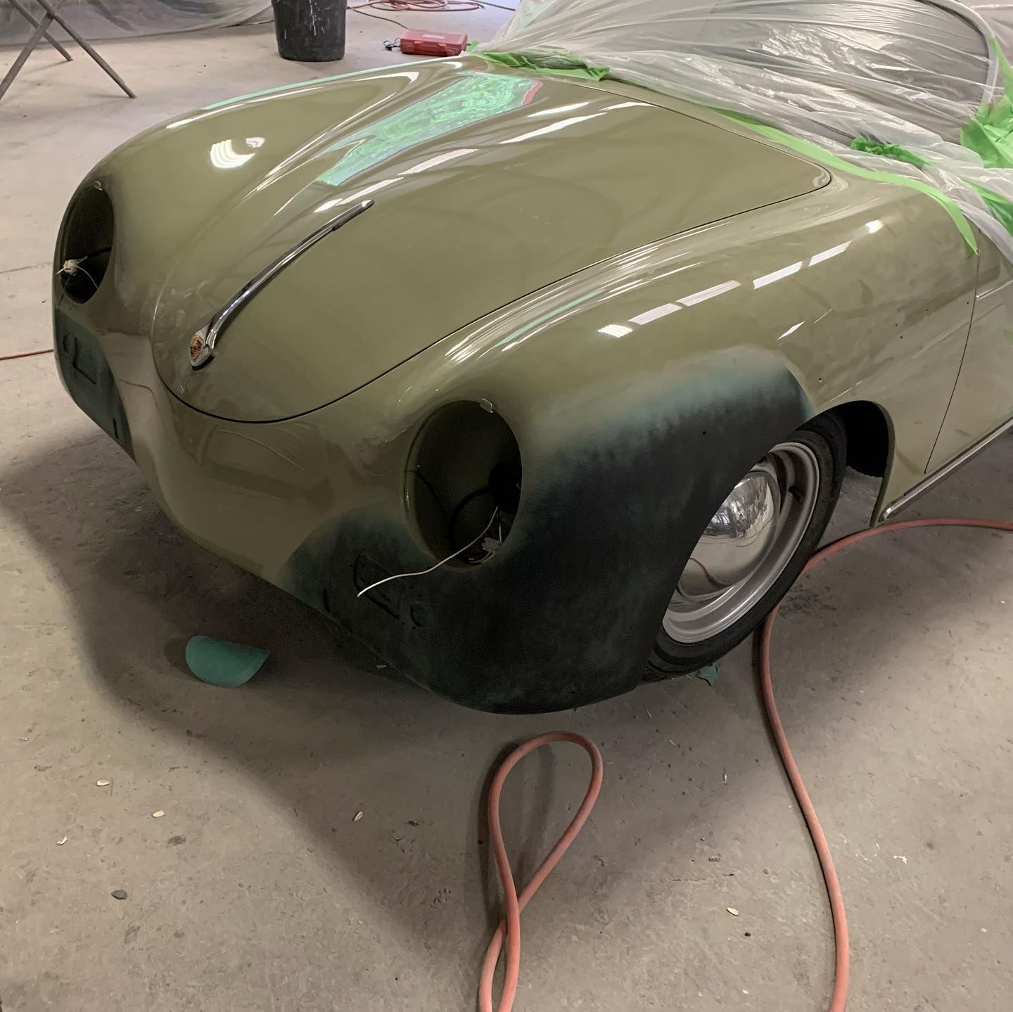 Car being restored, front end partially painted in green and gray, masked with plastic.