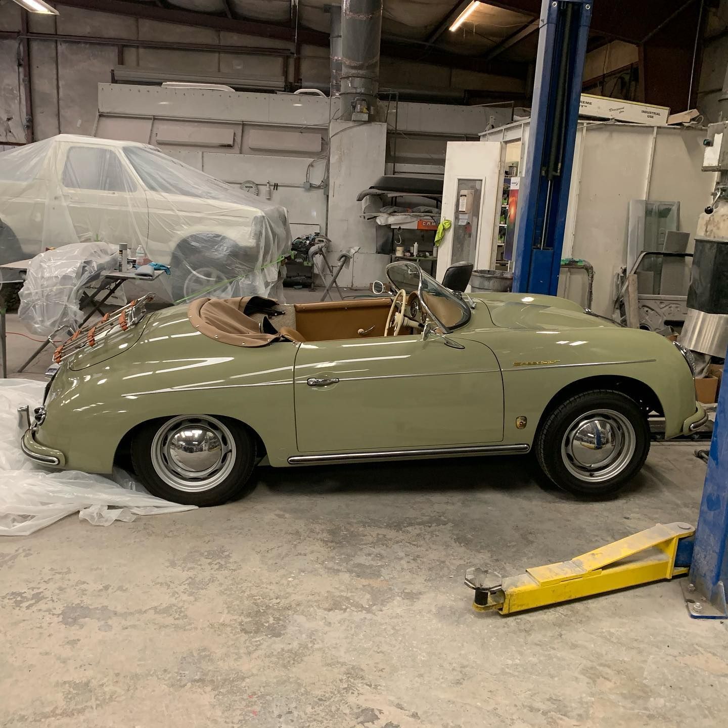 Sage green classic convertible car in a garage with a tan interior.