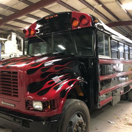Red and black school bus with flames painted on the front, parked indoors.