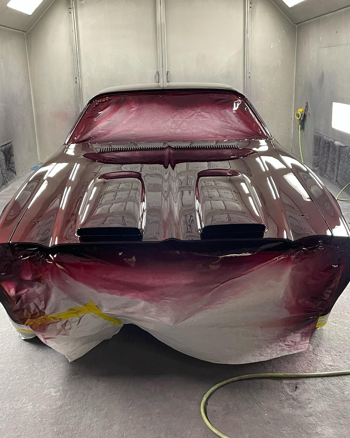 Car in a paint booth, covered in red primer, ready for paint.