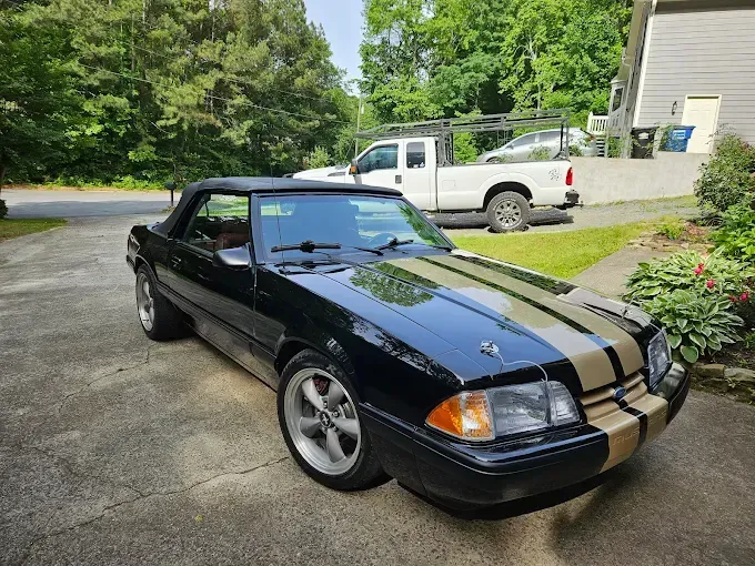 Black Ford Mustang convertible with tan racing stripes, parked on a driveway.