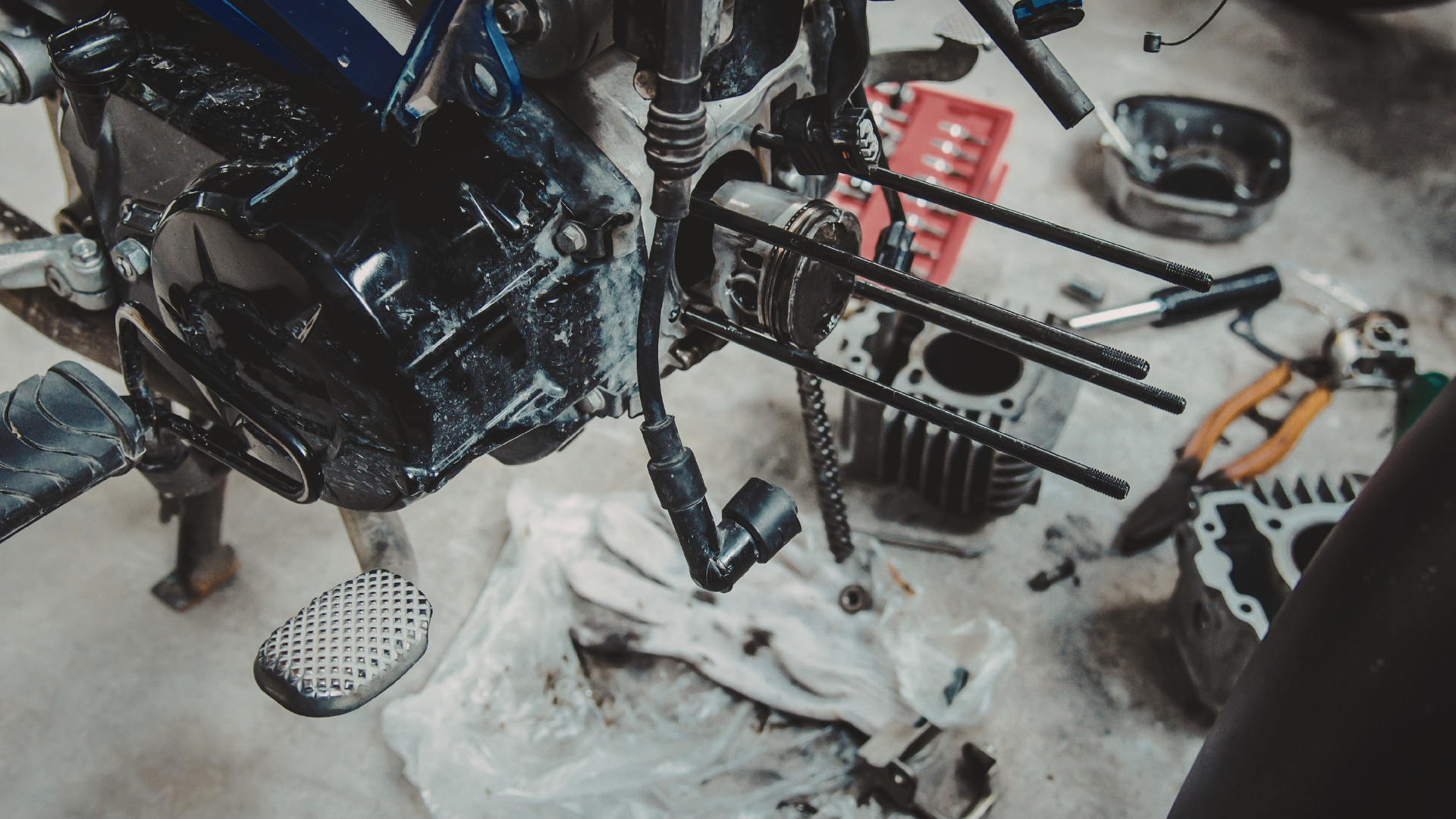 Motorcycle engine being repaired with tools and parts scattered on a surface.