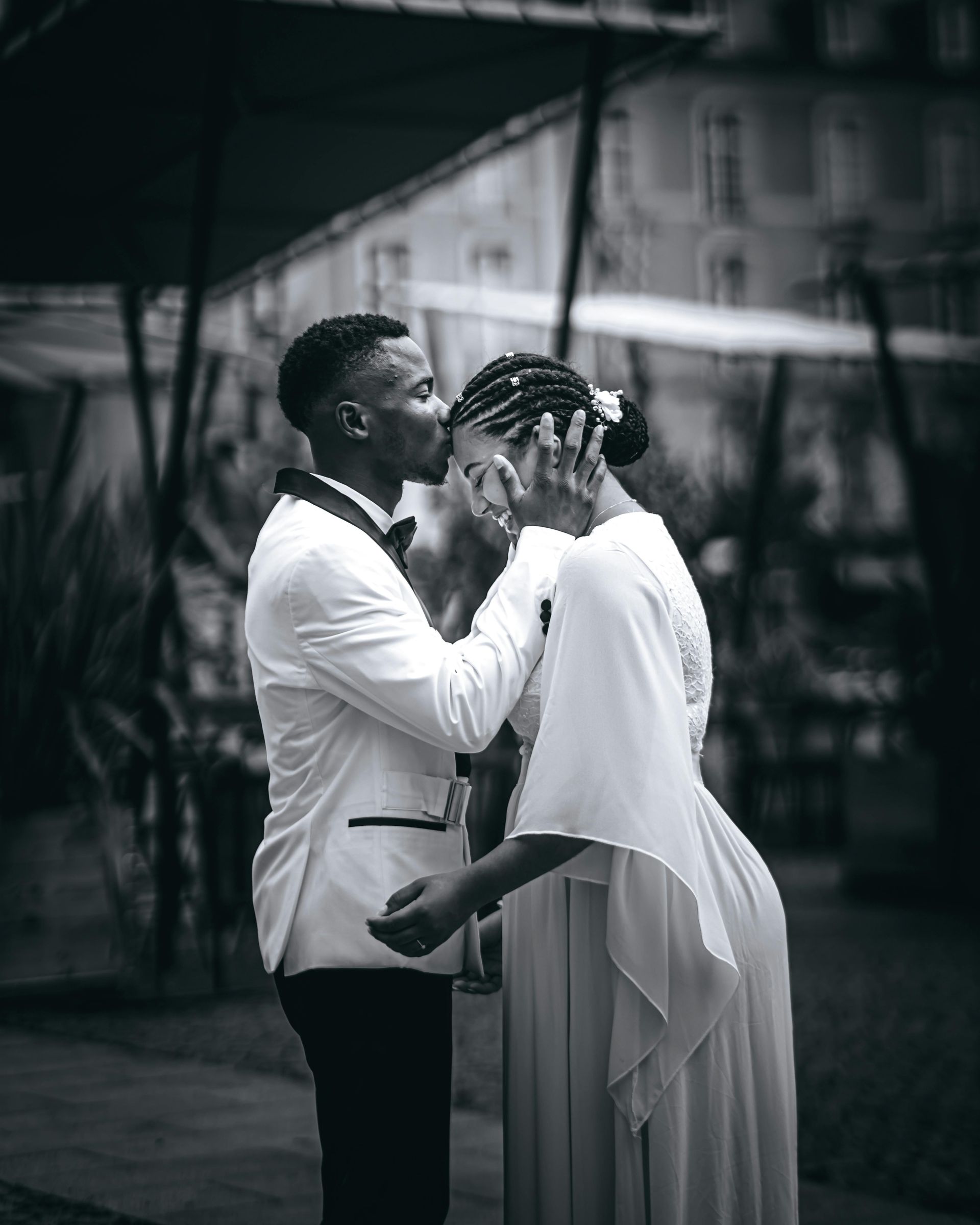 Black and white photo of a Black couple; the groom is touching the bride's forehead. They are outside, possibly on their wedding day.