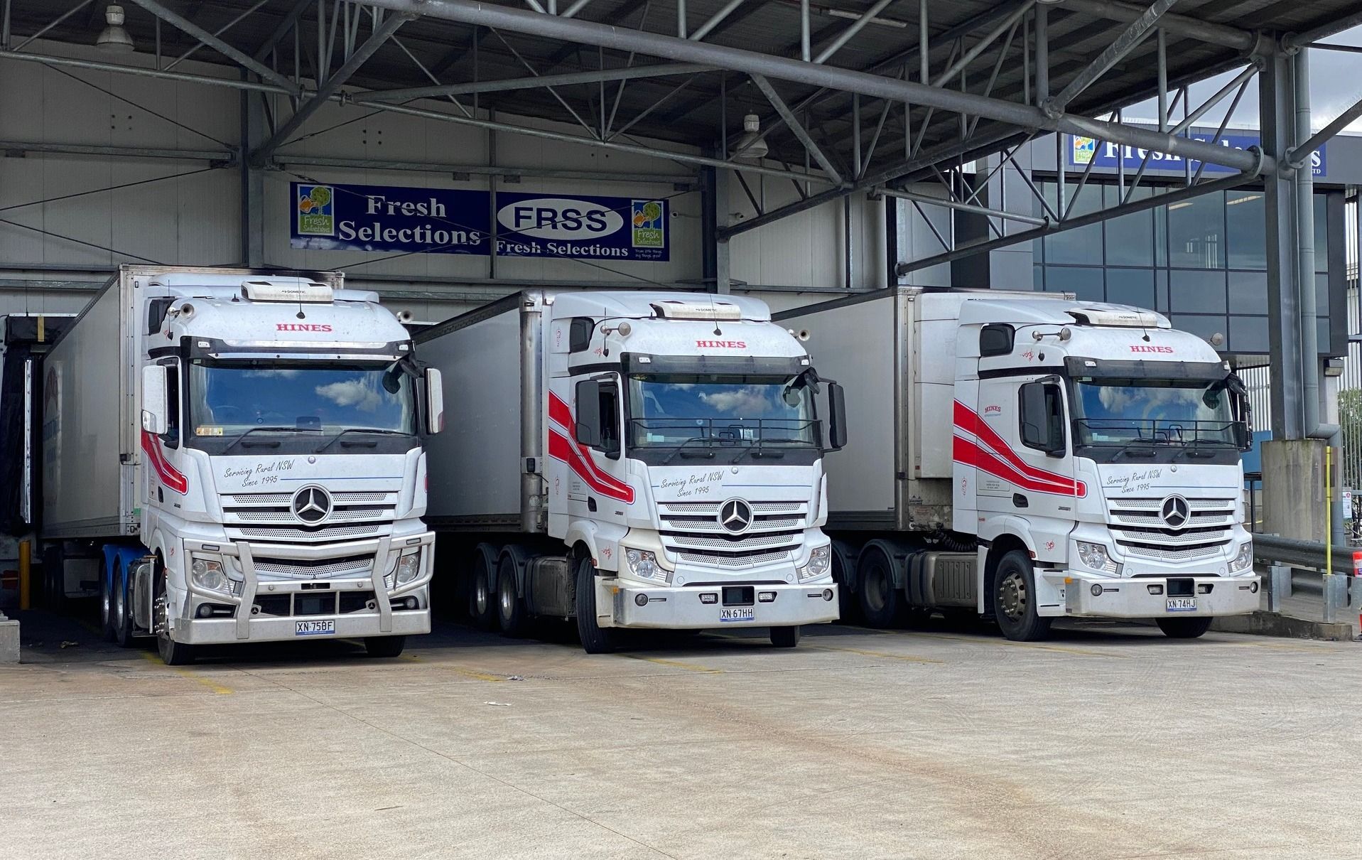 Three White Semi-trucks With Red Stripes Parked at a Loading Dock — Hines Logistic Pty Ltd In Kundabung, NSW