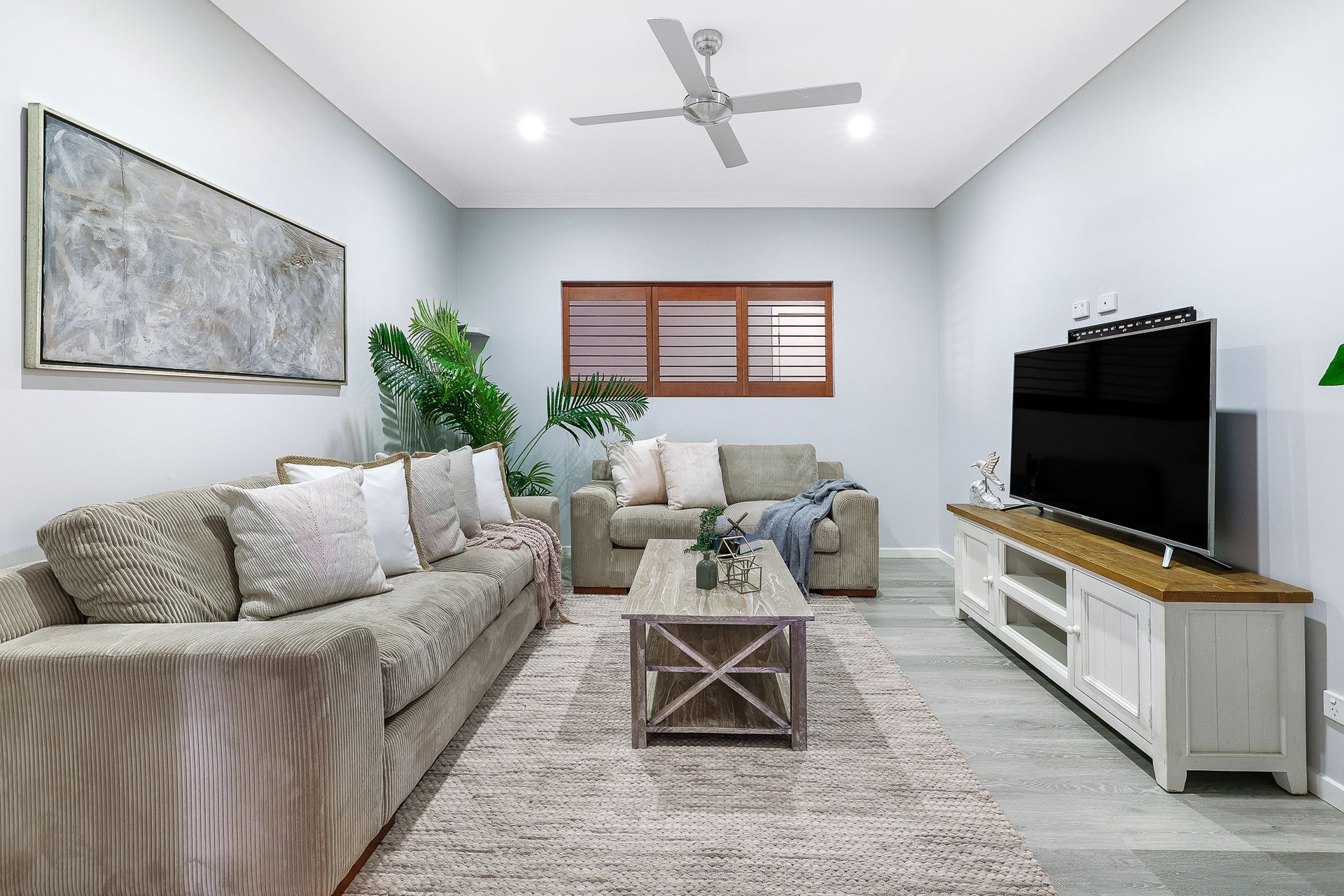 A living room with a couch , coffee table , television and ceiling fan.
