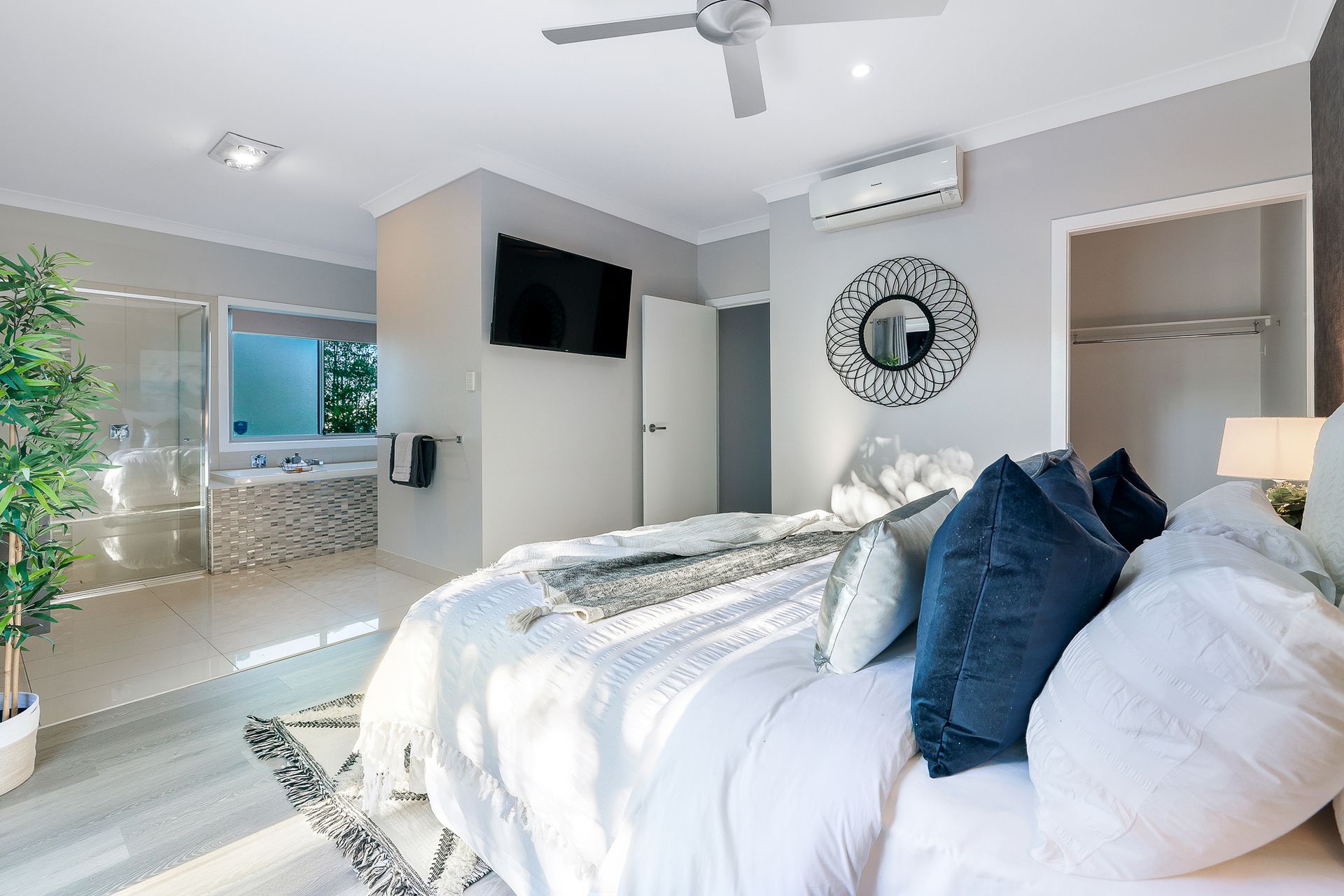A bedroom with a large bed , ceiling fan , television and bathtub.