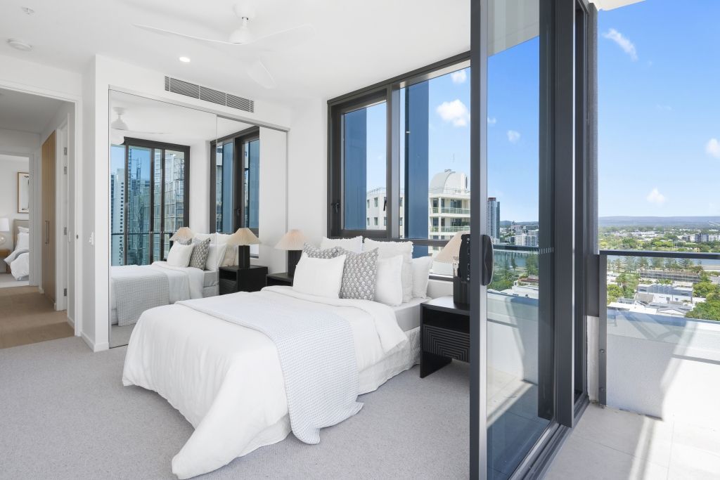 A bedroom with a large bed and a balcony with a view of the city.