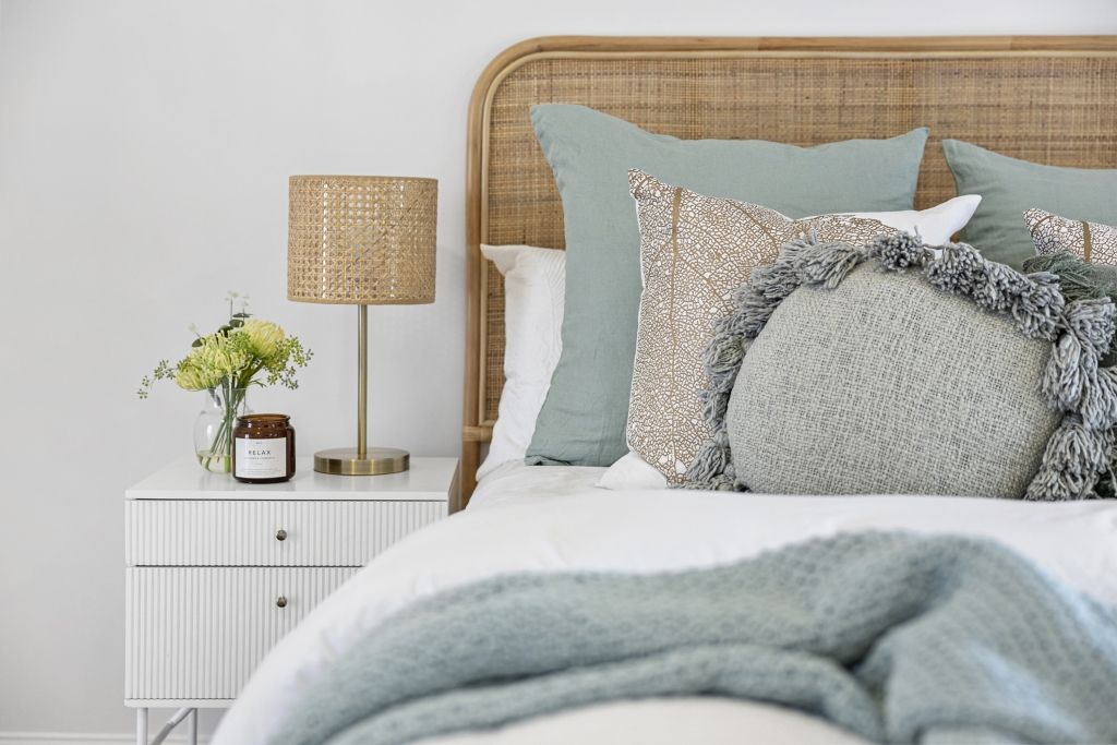 A bedroom with a bed , nightstand , lamp and pillows.