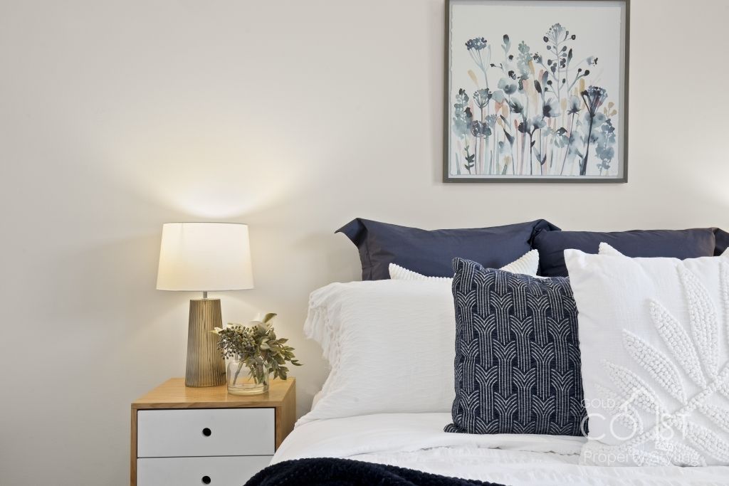 A bedroom with a bed , nightstand , lamp and painting on the wall.