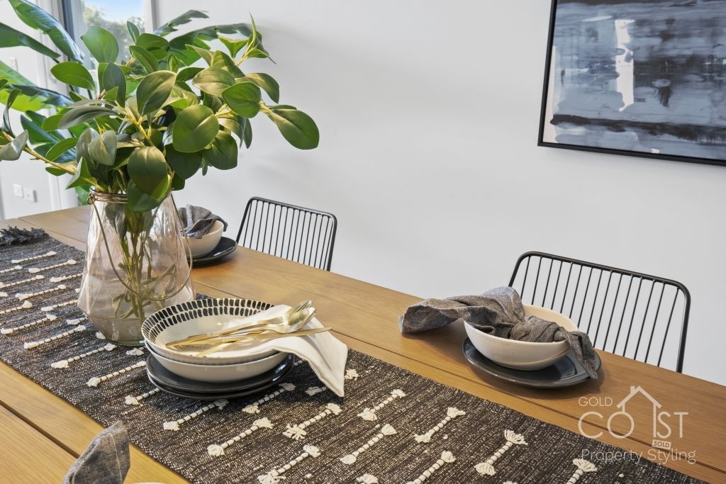 A dining room table with plates , bowls , and a vase of flowers on it.