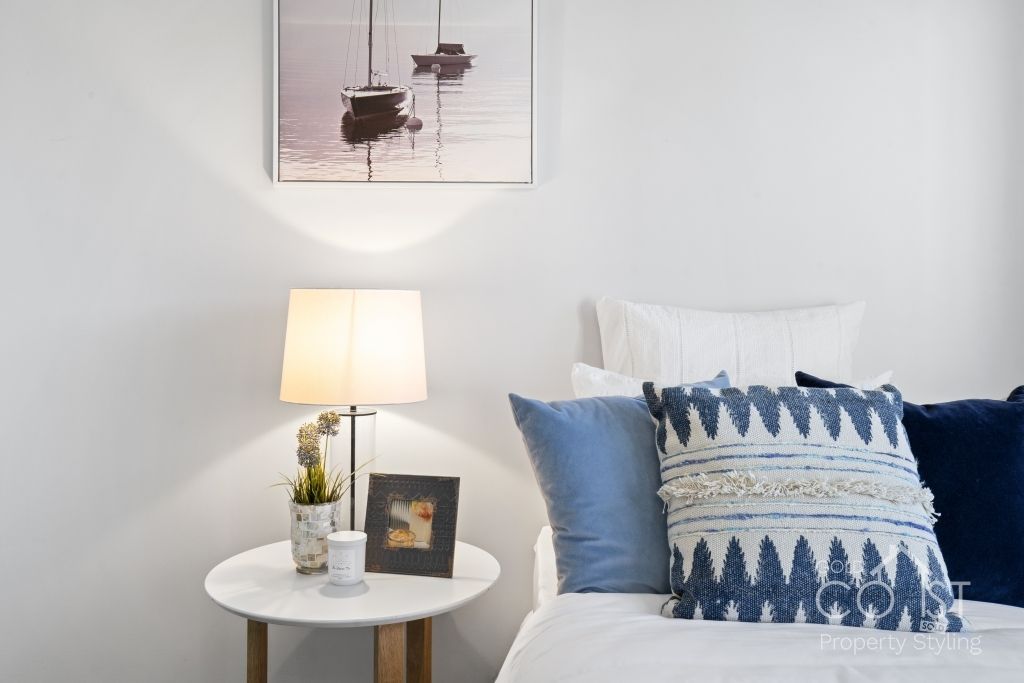 A bedroom with a bed , nightstand , lamp and painting on the wall.