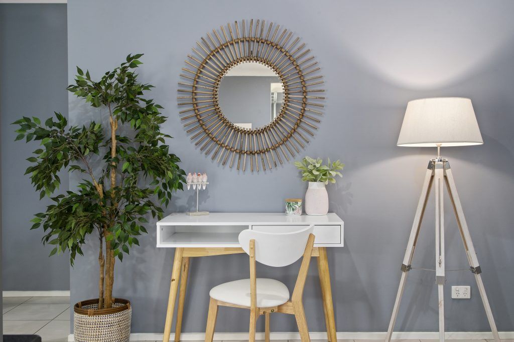 A room with a desk , chair , lamp , mirror and potted plant.