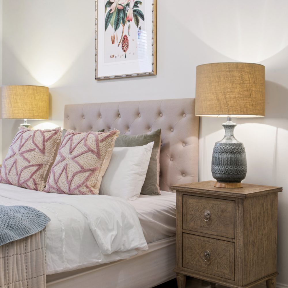 A bedroom with a bed , nightstand , lamps and a picture on the wall above the bed