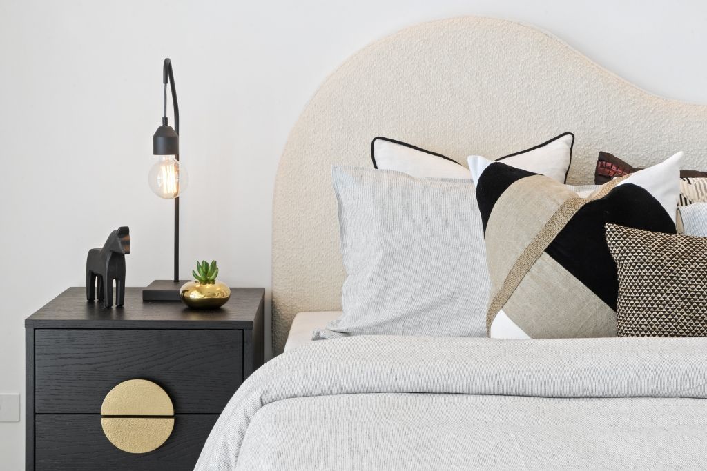 A bedroom with a bed , nightstand , lamp and pillows.