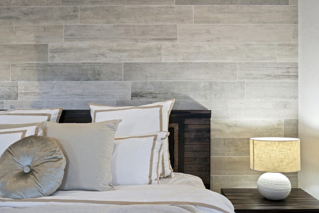 A bedroom with a bed , nightstand , lamp and a wooden wall.