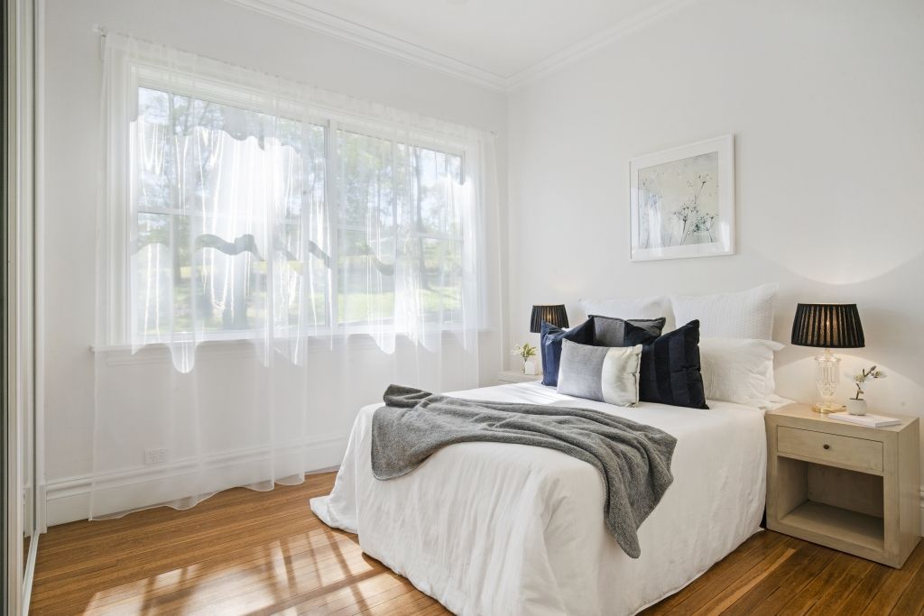 A bedroom with a bed , nightstand , lamps and a large window.