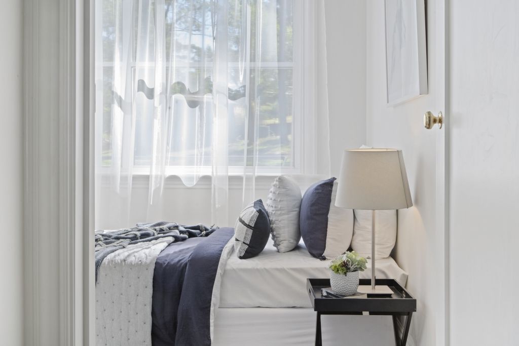 A bedroom with a bed , nightstand , lamp and window.