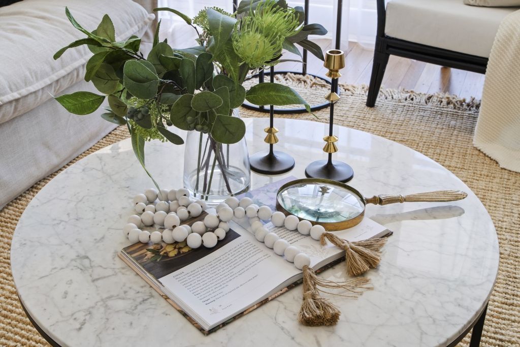 A round coffee table with a vase of flowers and a magazine on it.