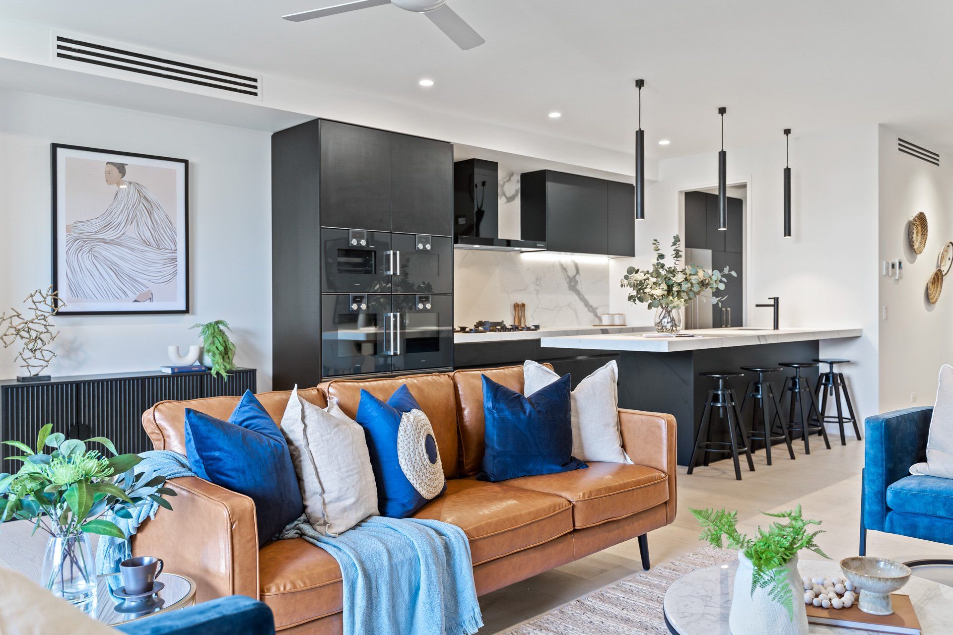 A living room with a brown leather couch and blue pillows.