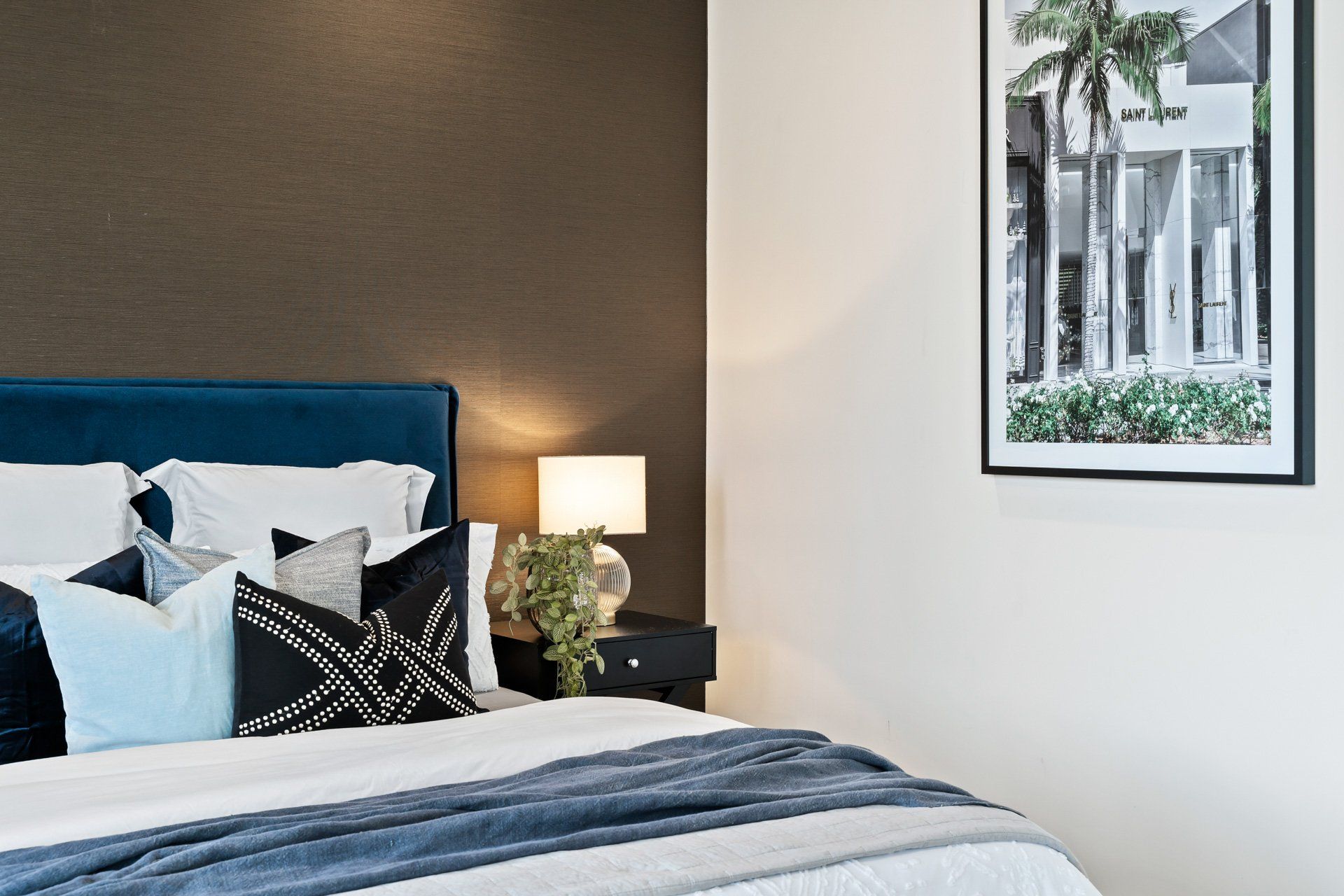 A bedroom with a bed , nightstand , lamp and picture on the wall.