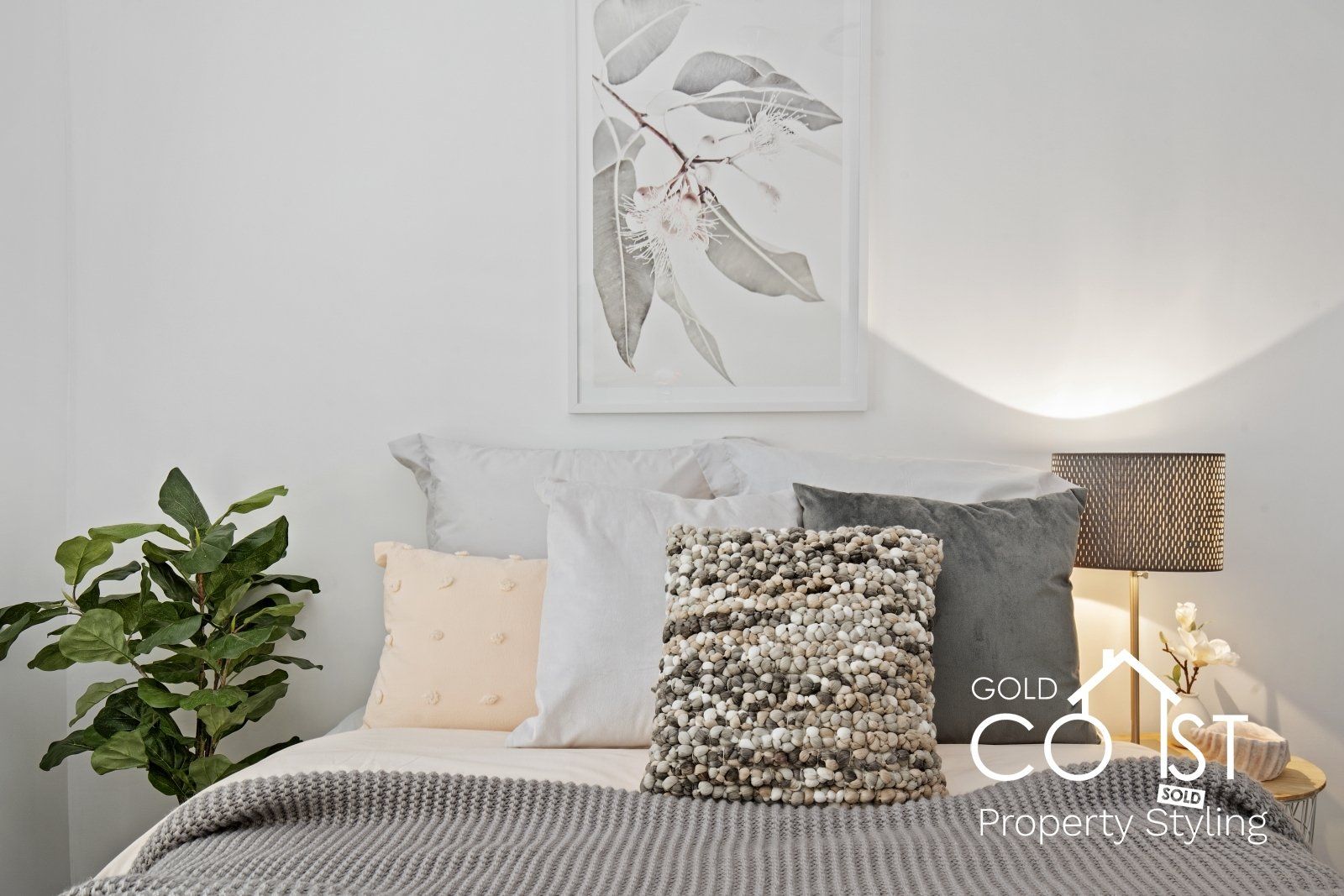 A bedroom with a bed , pillows , a lamp and a painting on the wall.