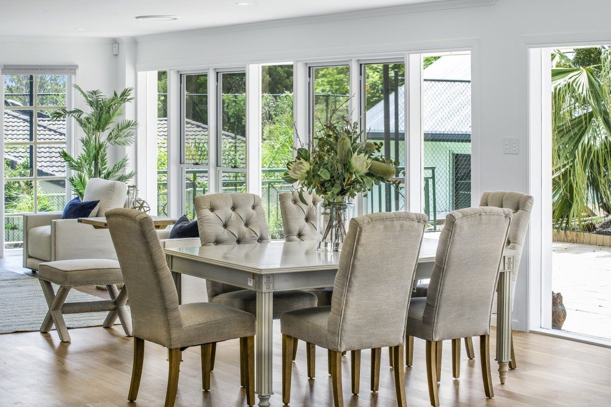 A dining room with a table and chairs and a vase of flowers.