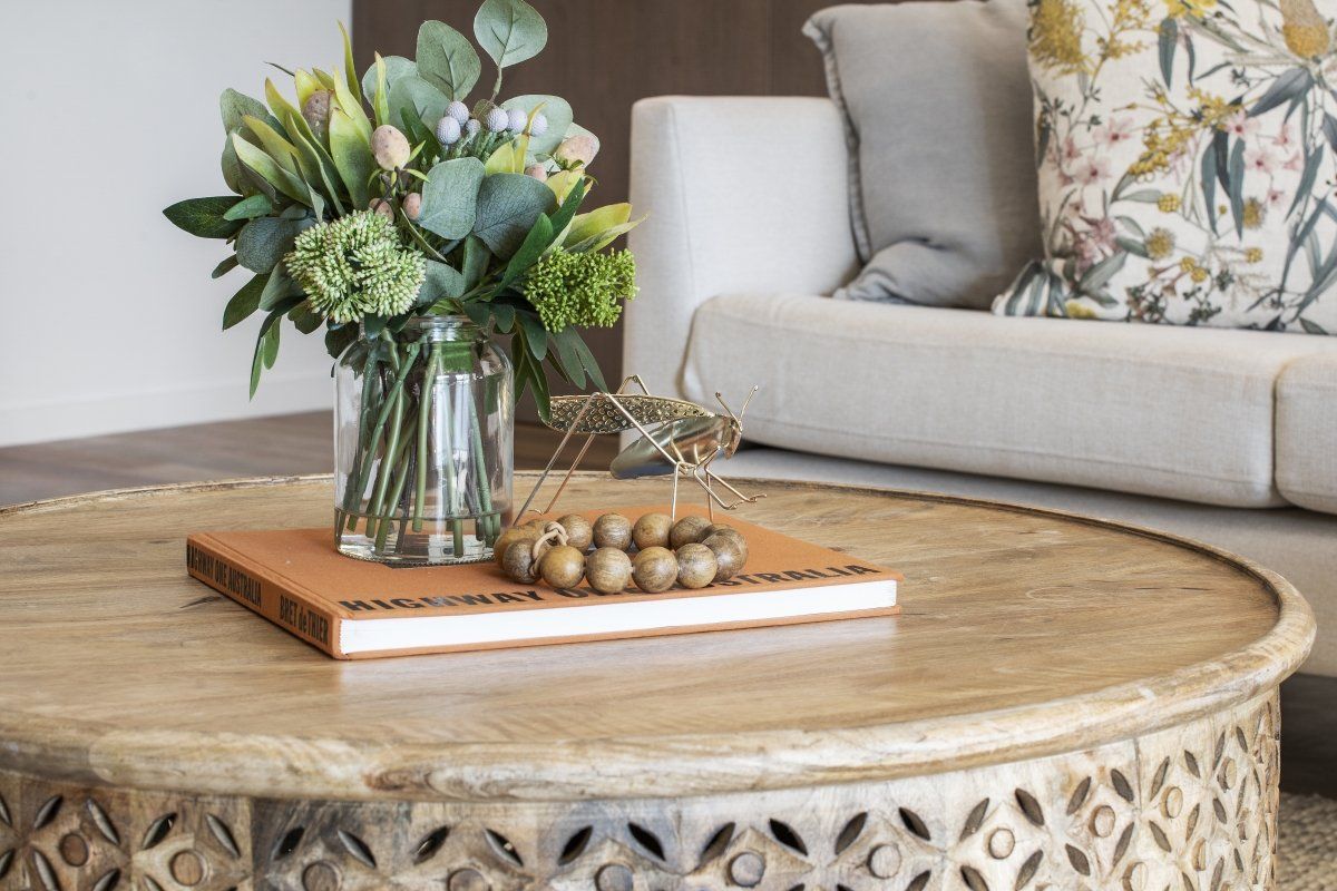 A coffee table with a vase of flowers and a book on it in a living room.
