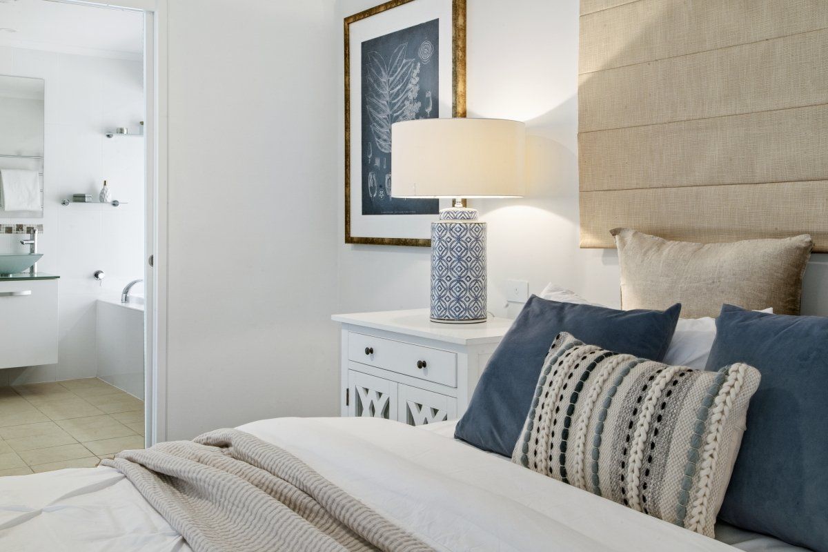 A bedroom with a bed , nightstand , lamp and pillows.