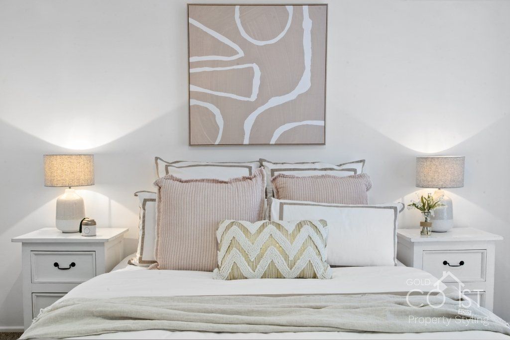 A bedroom with a bed , nightstands , lamps and a painting on the wall.