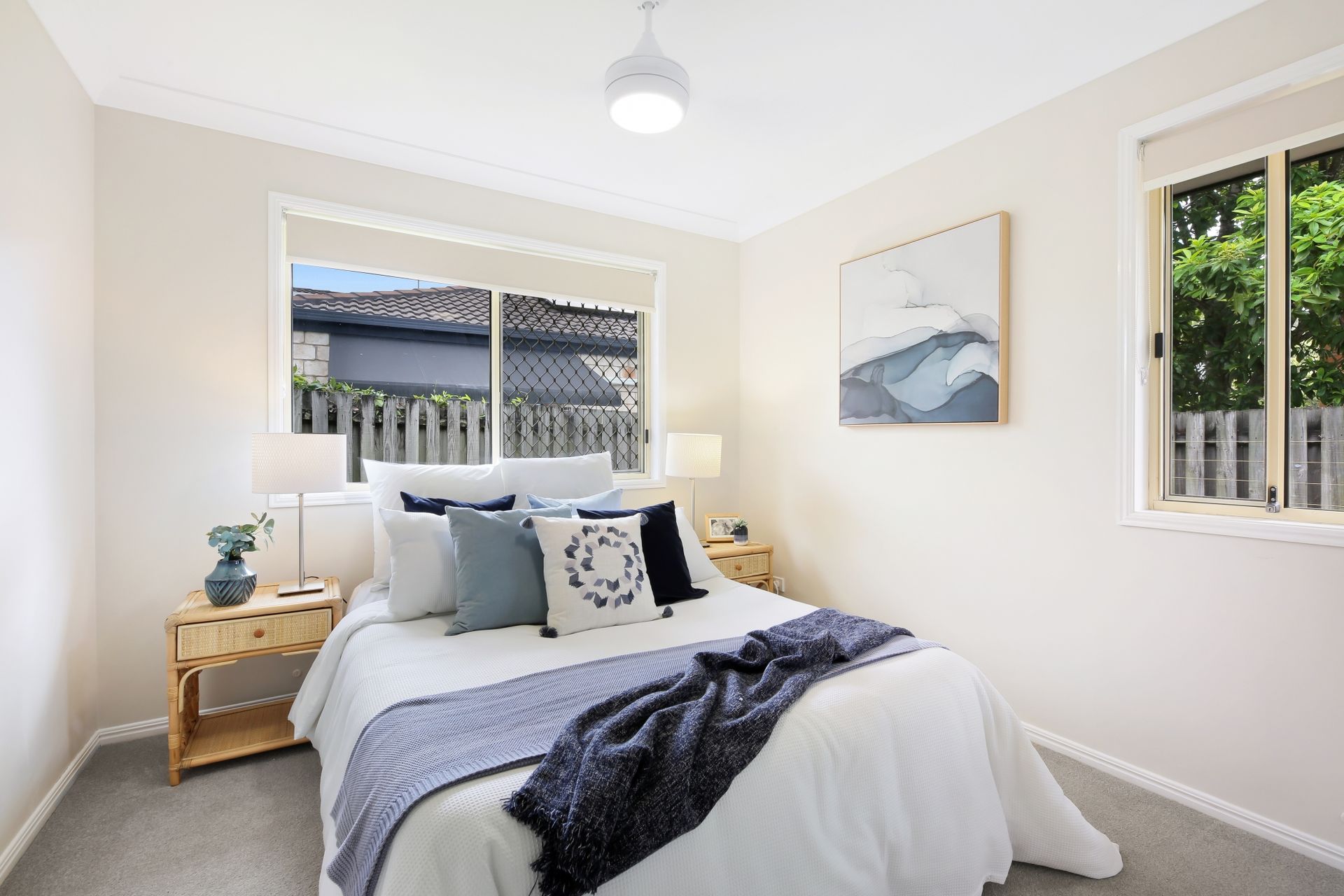 A bedroom with a bed , two nightstands , a window and a painting on the wall.