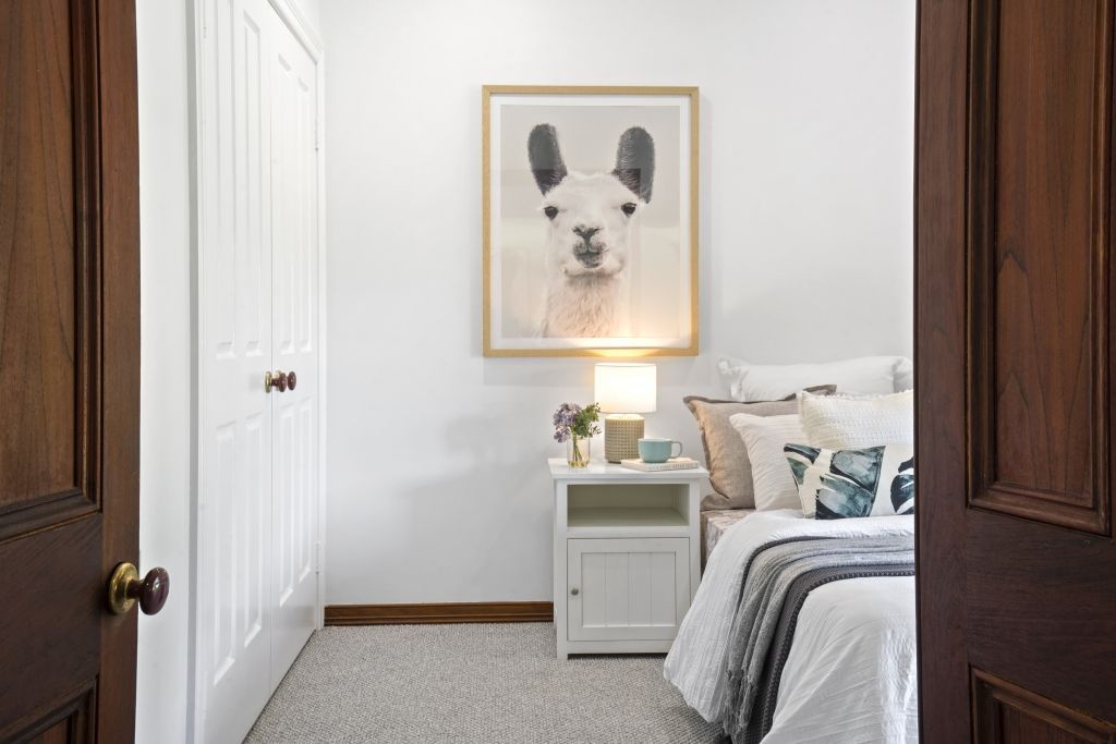 A bedroom with a bed , nightstand , and a painting of a llama on the wall.