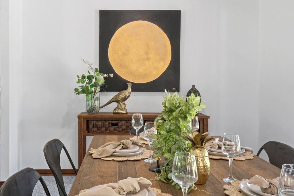 A dining room table with plates , glasses , and a painting on the wall.