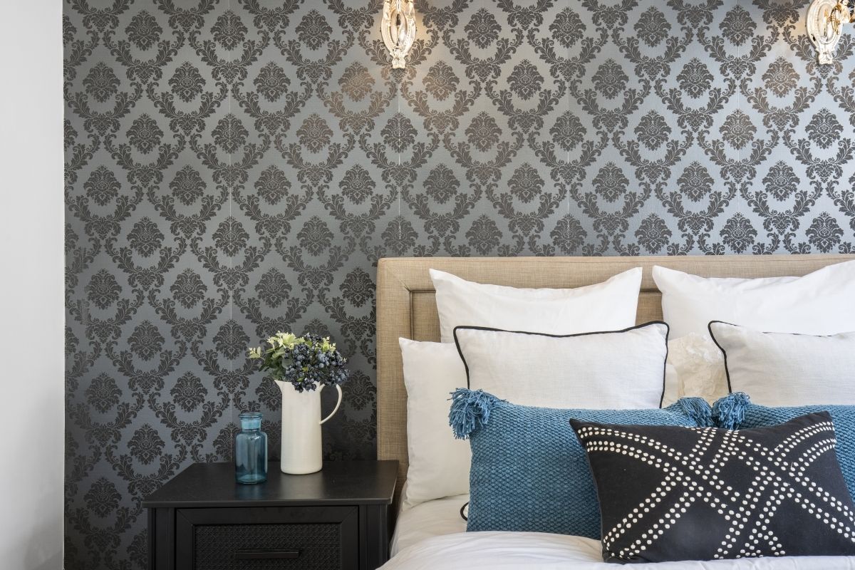 A bedroom with a bed , nightstand , and wallpaper on the wall.