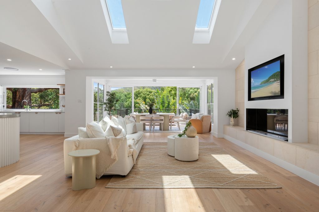 Bright modern living room with skylights, white sofas, a fireplace, and large windows overlooking greenery