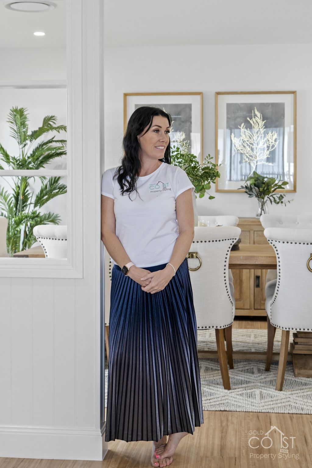 A woman in a white shirt and blue skirt is standing in a dining room.
