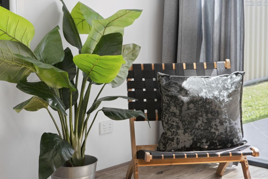 A chair with a pillow and a potted plant next to it.