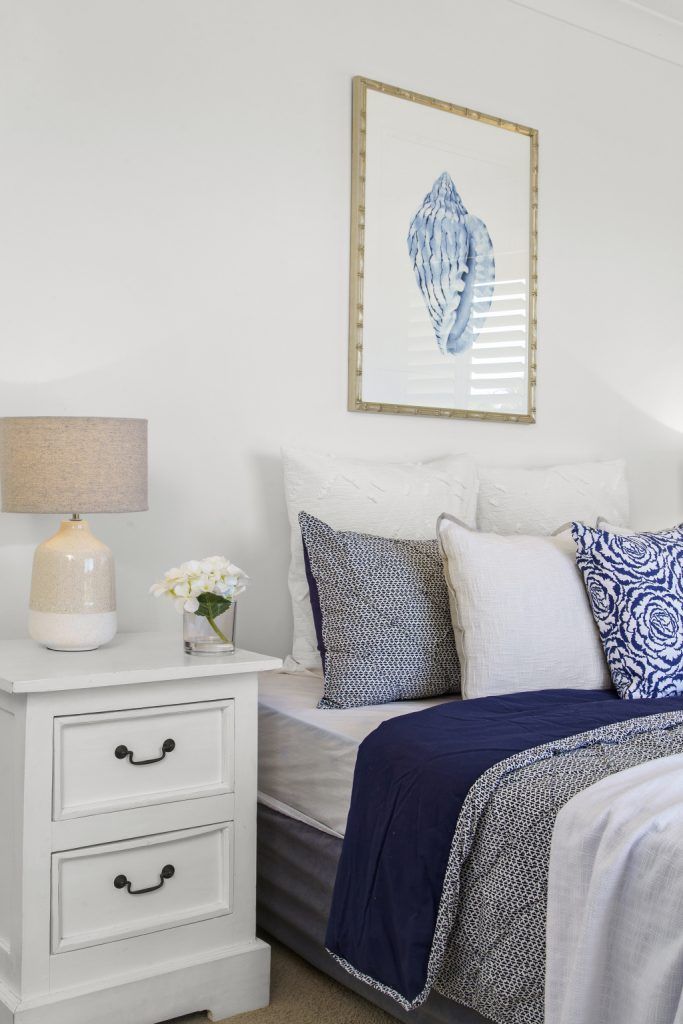 A bedroom with a bed , nightstand , lamp and painting on the wall.