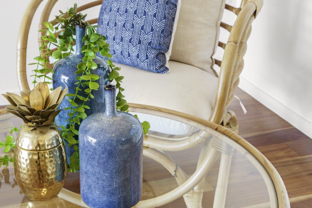 A wicker chair is sitting next to a glass table with vases on it.