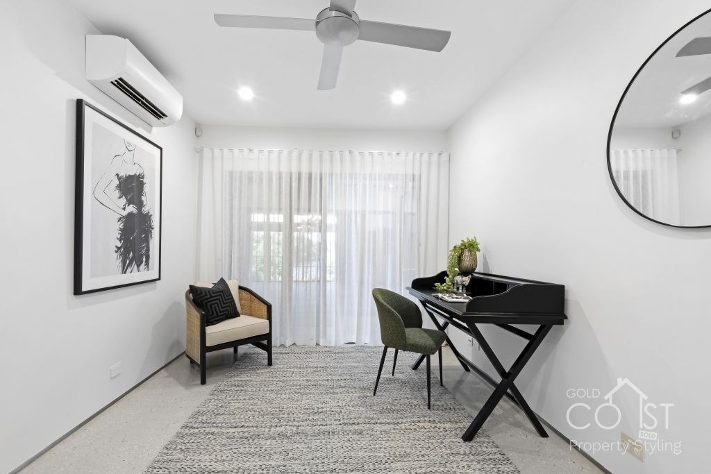 A living room with a ceiling fan , chair , desk and mirror.